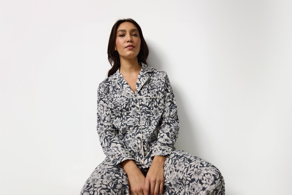 Person wearing long-sleeve button-up pyjamas with a black and white floral print, sitting against a plain white background.