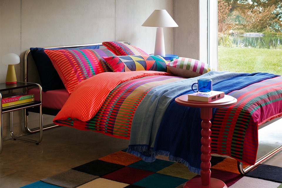 Colourful bold bedroom with striped colourful bedding and bobble side table in red and white lamp.