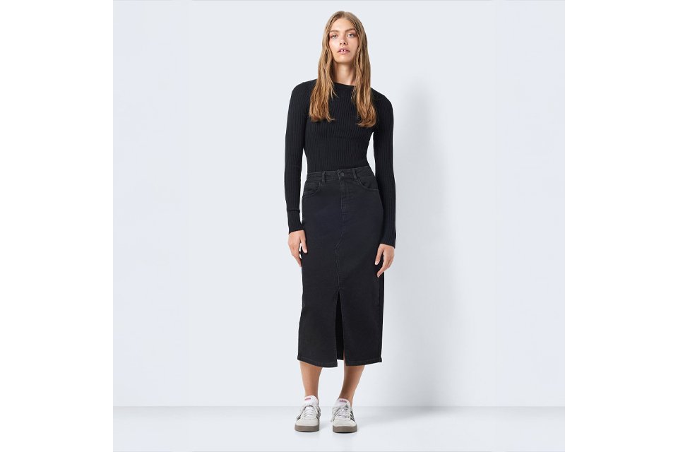 Person wearing a black long-sleeve ribbed top paired with a high-waisted black denim midi skirt featuring a front slit, styled with white sneakers. 