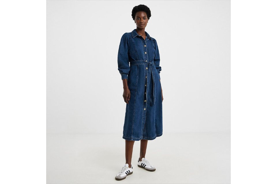 Person wearing a long-sleeve button-down denim midi dress with a matching tie belt at the waist, styled with white and black sneakers. 