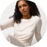 Person wearing cream-coloured long-sleeve pyjama set with subtle pink heart print, sitting against a plain white background.