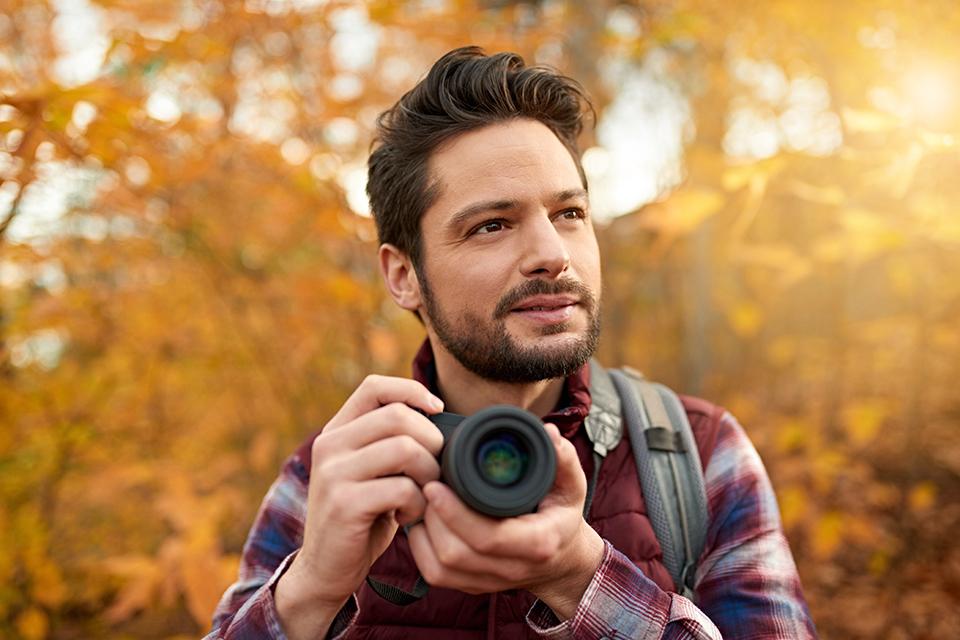 Man in forest taking photograph with a mirrorless camera.