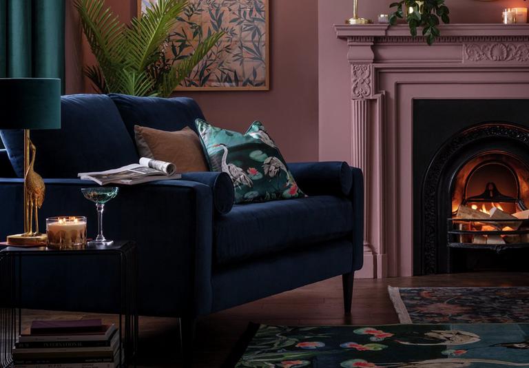 Image of a navy velet sofa in a dusky pink living room by a fire.
