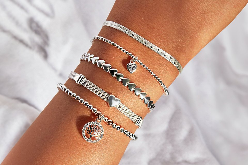 Five silver bracelets, including some with charms, on a person's hand.