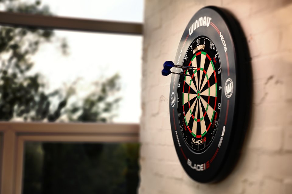 Two darts on a Winmau dartboard hanging on a brick wall.