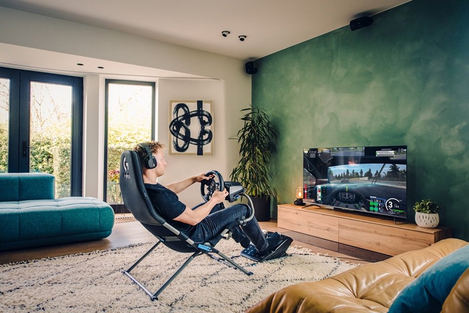 A man using Playseat Challenge X Logitech G Edition in black colour to play a racing game on a gaming console.
