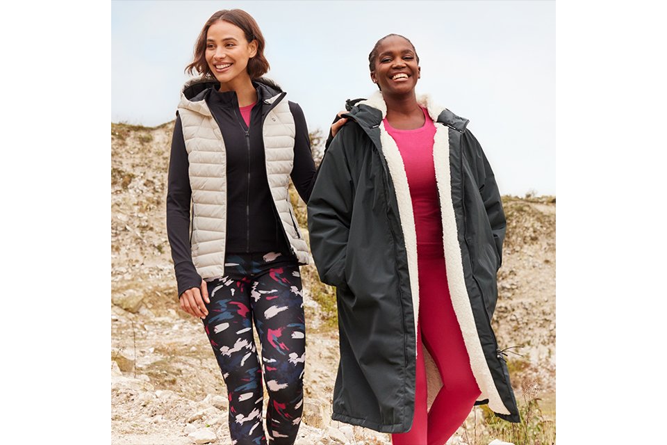 Two people walking outdoors on rocky terrain, wearing activewear with layered outerwear.
