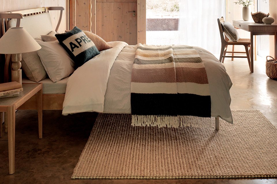 A beige striped rectangular rug under a bed in a bedroom.