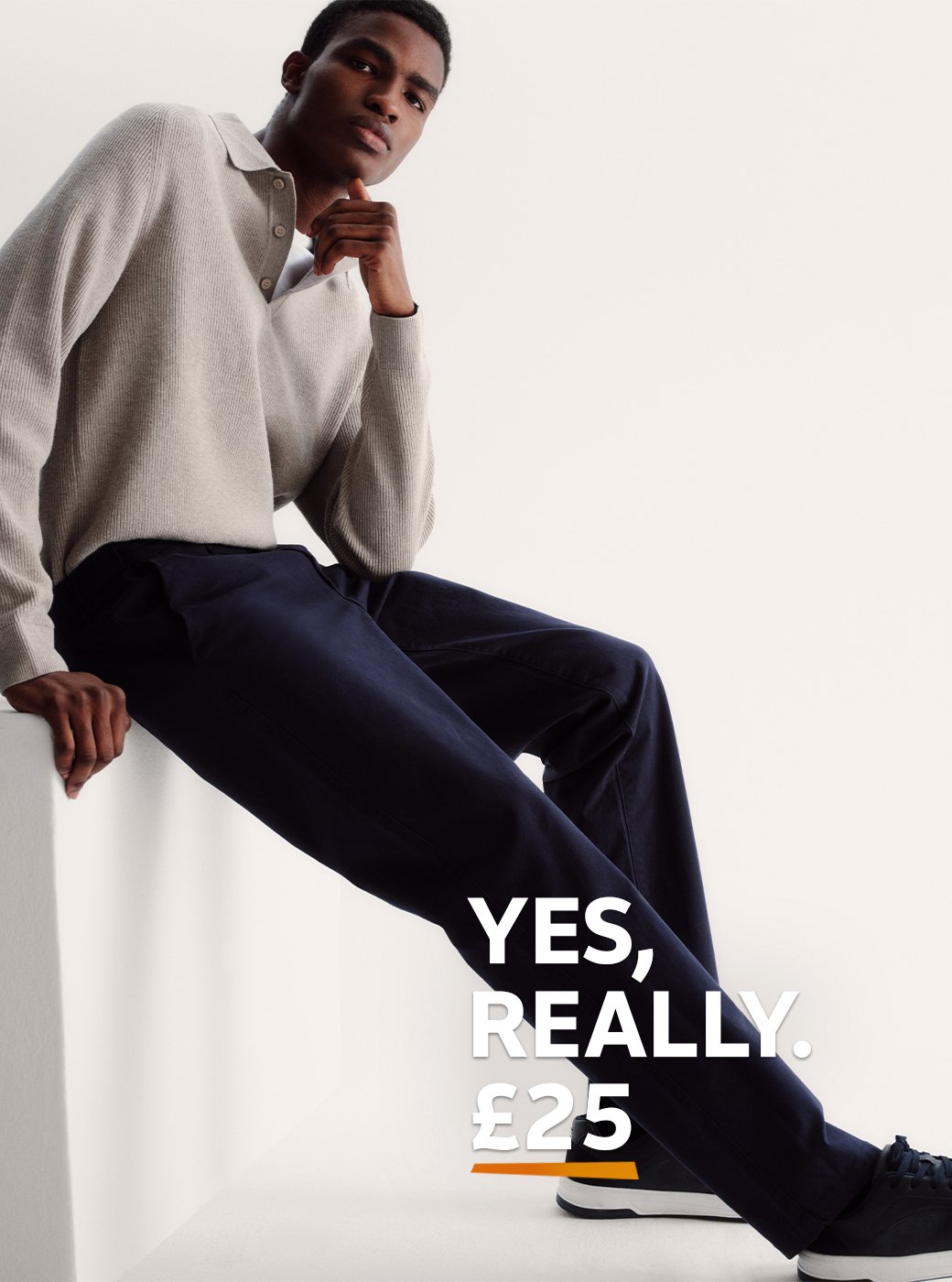 A man wearing navy chinos, with trainers and a neutral jumper. 