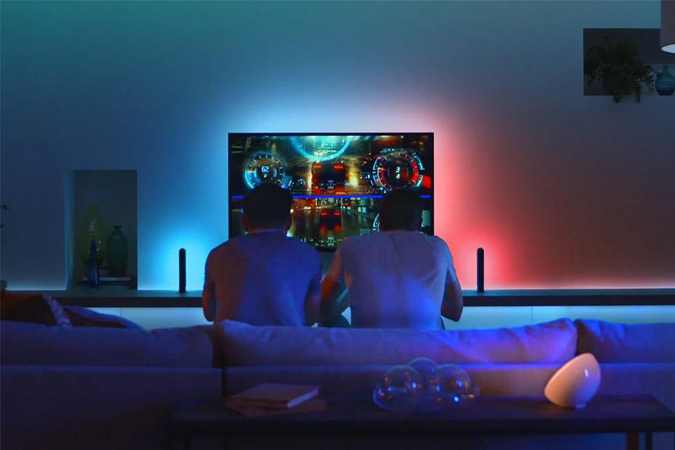 Two men gaming with Philips Hue lights behind TV matching the on-screen content.