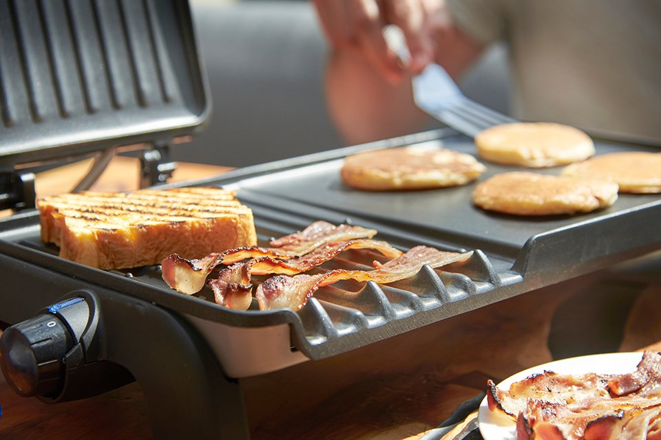 A person grilling breads and meat on a George Foreman grill.