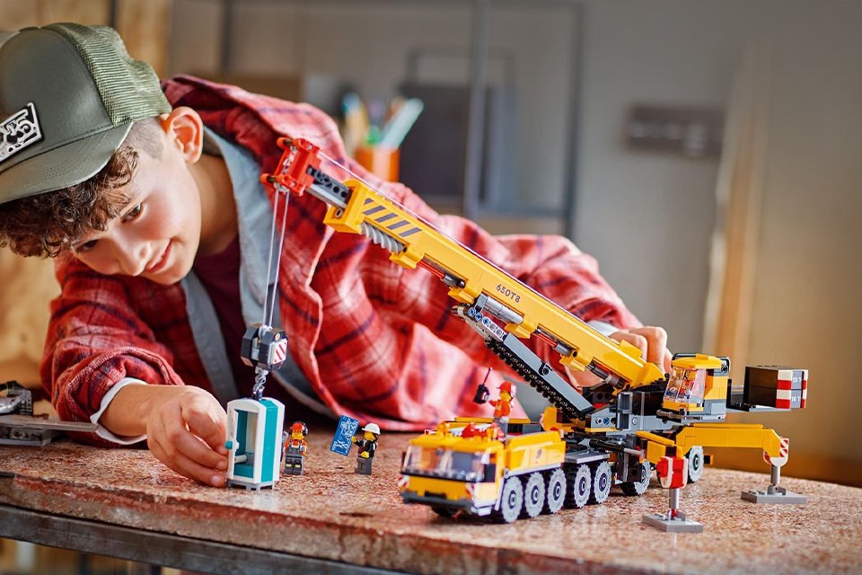 A boy playing with LEGO City Yellow Mobile Construction Crane Toy Set.