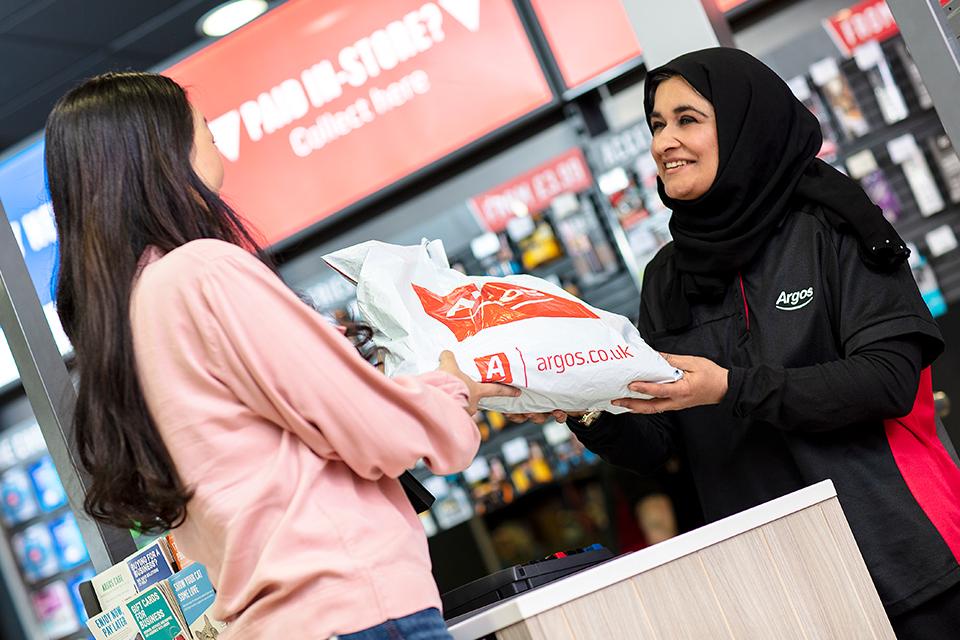 Argos employee passing over a package to a customer in store.