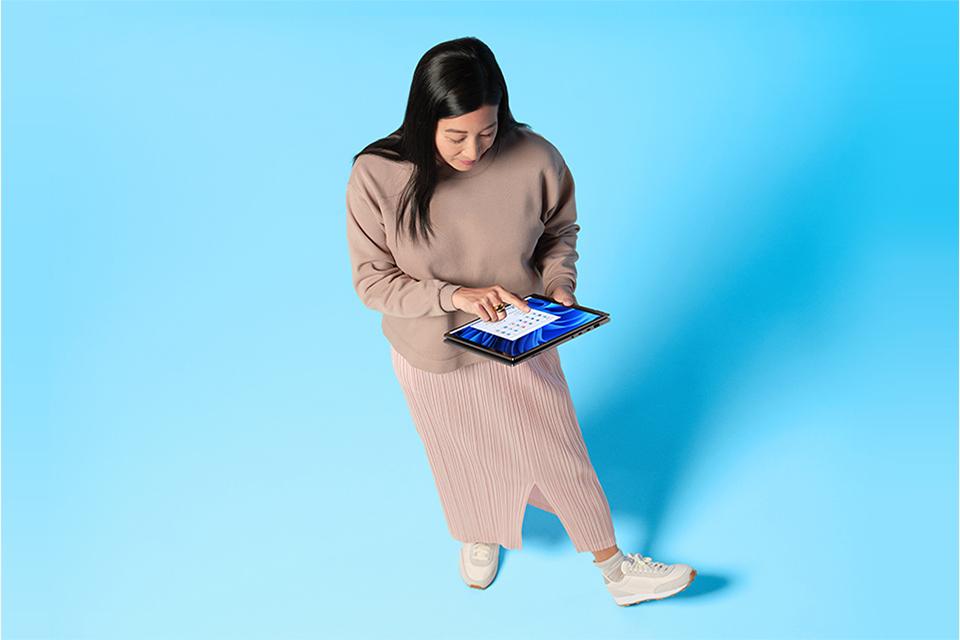 Young woman stands holding  a tablet.