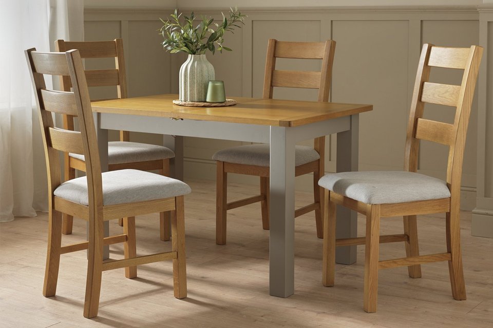 A vase and a candle on an Argos Home Ashwell Ext Oak Dining Table surrounded by 4 chairs.