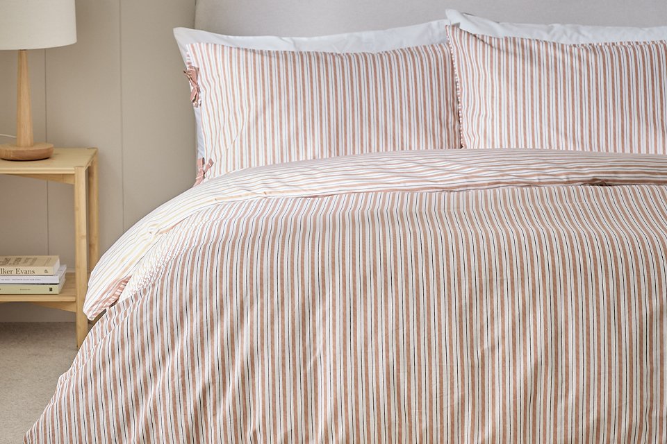 Stripe bedding on cream headboard in bedroom.