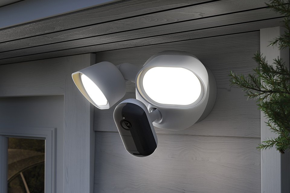 A pair of Arlo wired floodlight placed outside a home and switched on.
