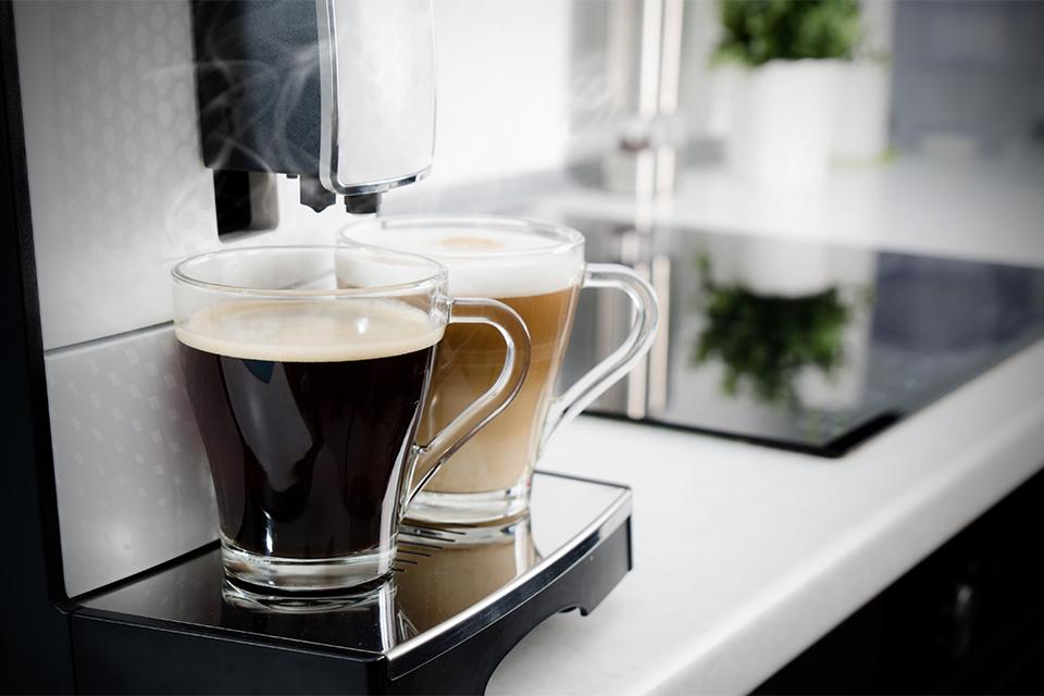 2 fresh cups of hot coffee being made by a coffee machine on a kitchen worktop.