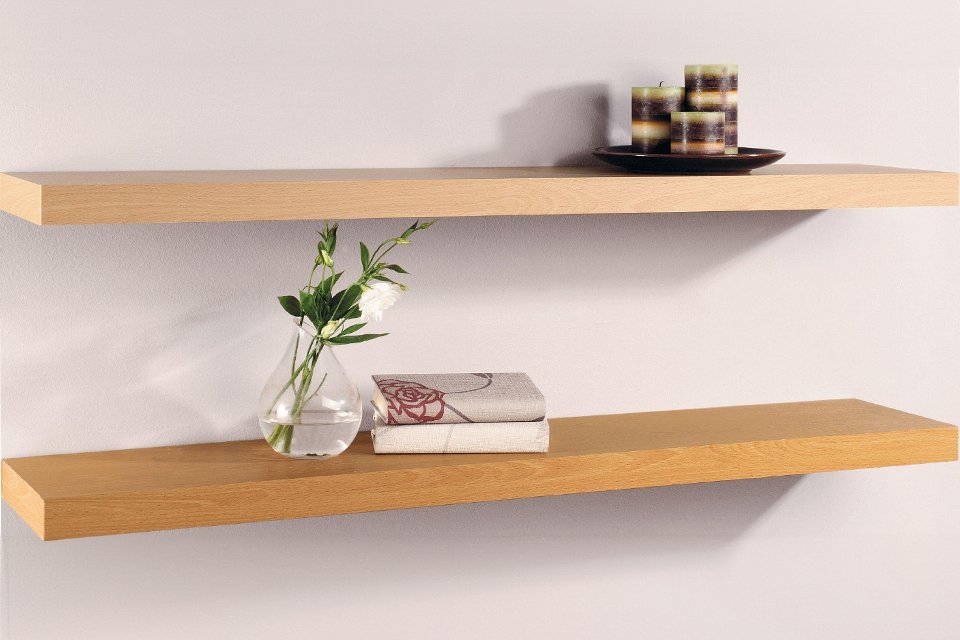 A pair of wooden shelves with a vase, books and candles on it. 