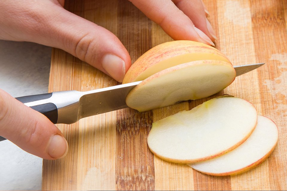 A paring knife being used to finely slice an apple.