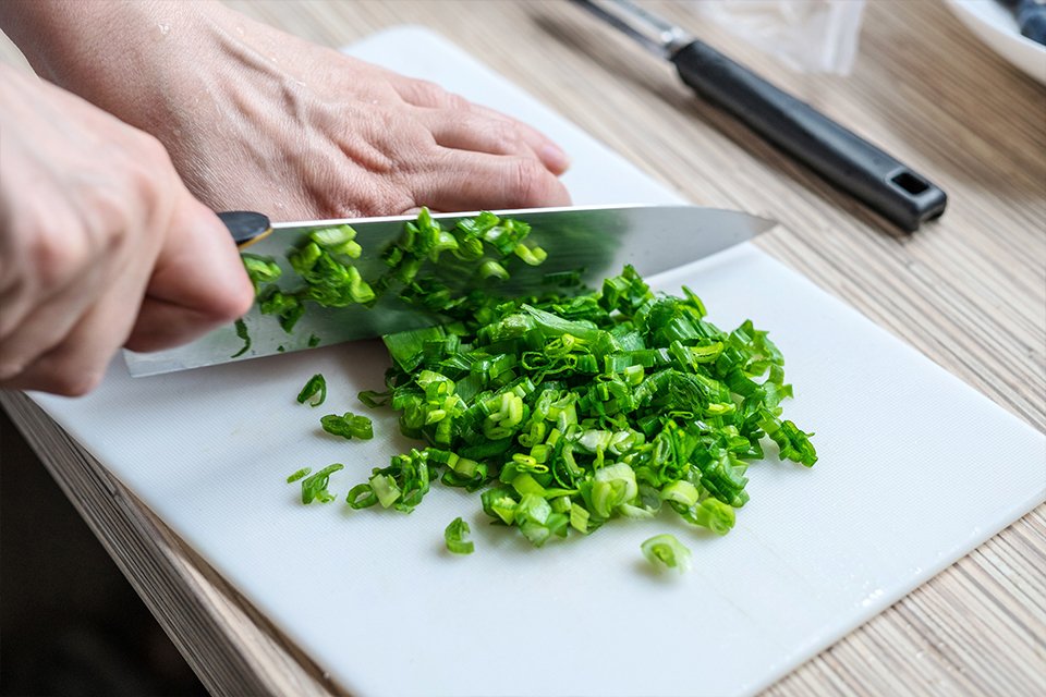 A chef's knife being used to chop up green onions.