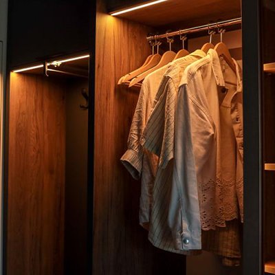 A wooden finish wardrobe with yellow cabinet lights in it.