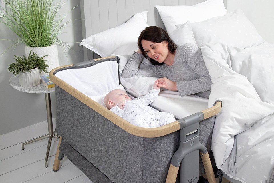 A mother sleeping next to a baby in a bedside crib.