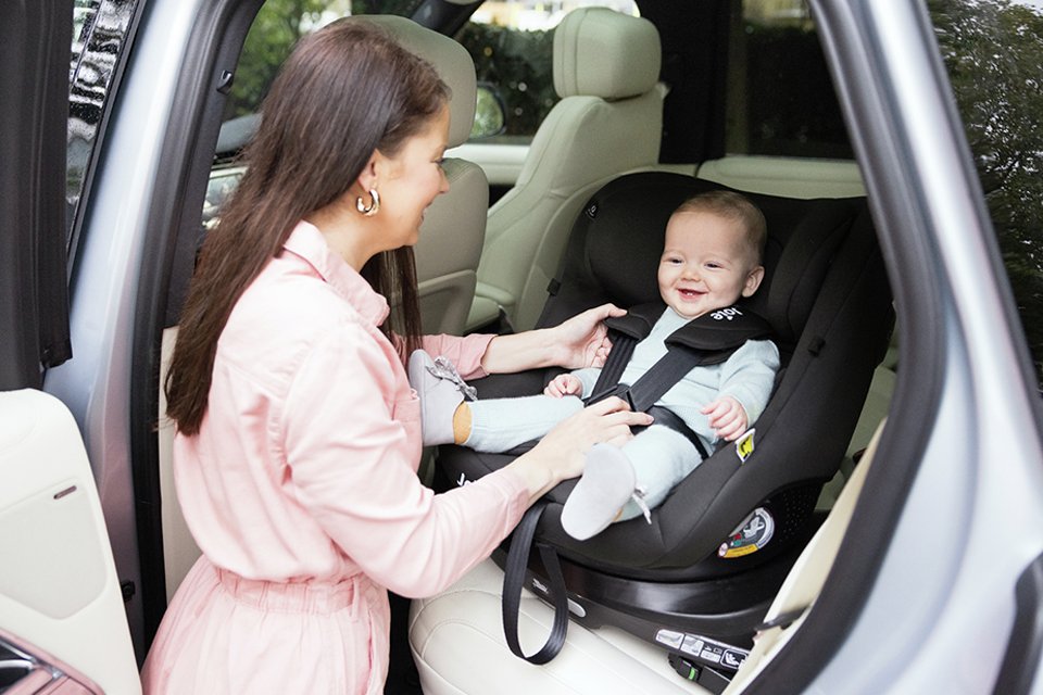 A mum ensuring her baby is fastened well in a Joie i-Pivot 360 spinning car seat.