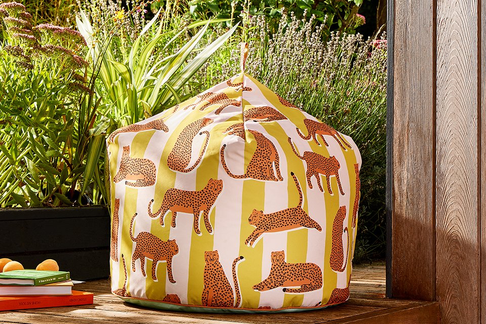 Outdoor Scion x Habitat colelction bean bag with yellow and white strips with leaopard print layered over stripes, in a garden corner next to planters perfect for an outdoor reading spot.