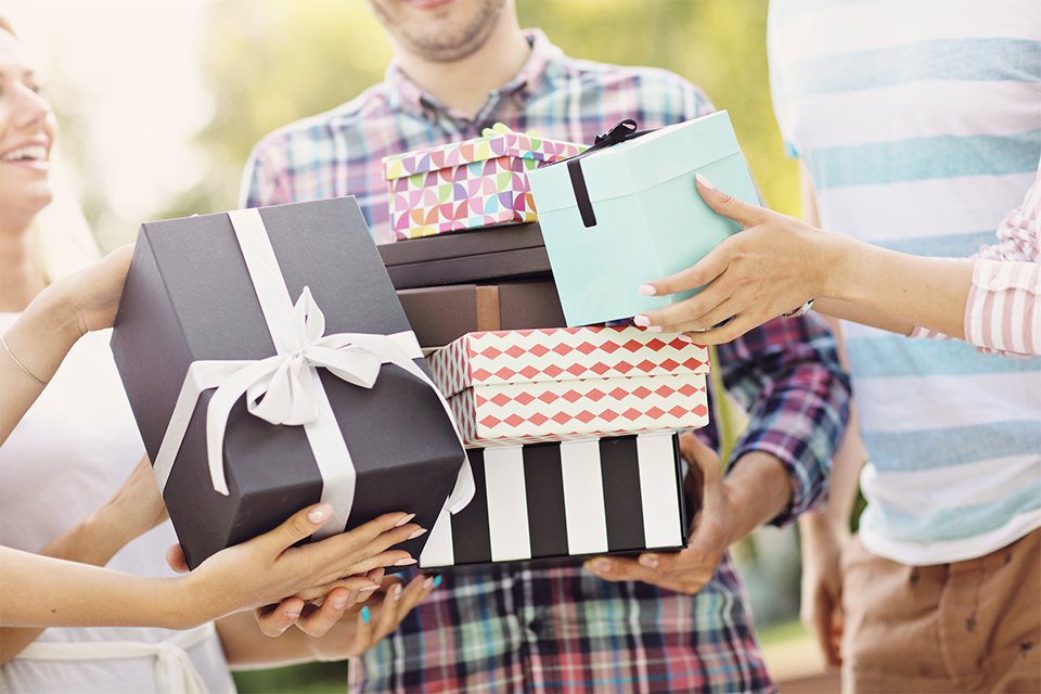 A man holding several presents while his friends pile even more into his arms.