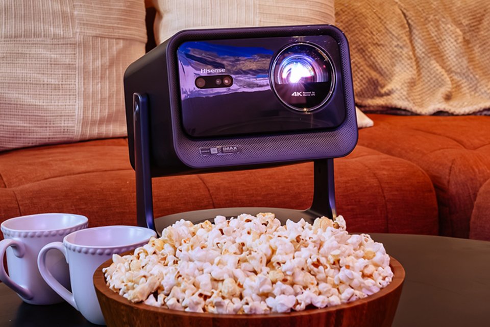 Hisense laser projector placed on a table next to cups and bowl of popcorn.