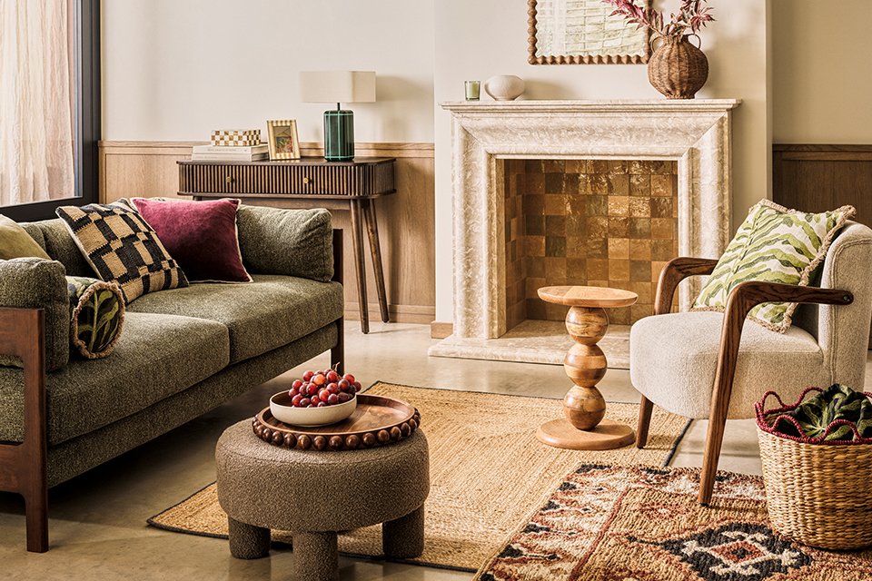 Neutral living room with light green velvet sofa with dark wooden arms and white accent chair in corner with wooden arms and touches of florals and woven basket on top of a persian rug.