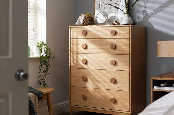 Tall oak chest of drawers with print and plant on top.