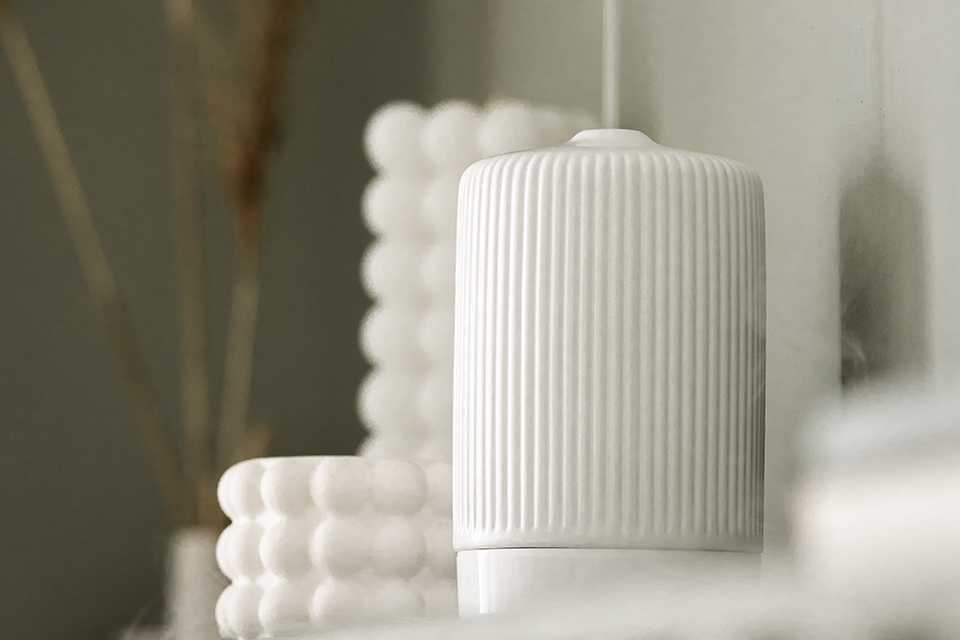 A white diffuser placed next to white candles.
