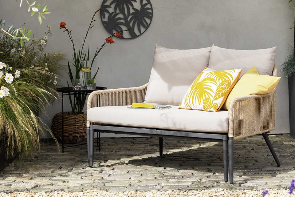 A yellow pillow and a two-seater sofa in a garden.