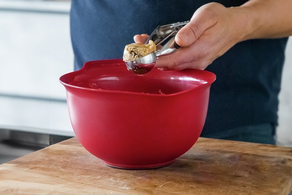 A person mixing cookie dough in a KitchenAid set of three mixing bowls in empire red colour.