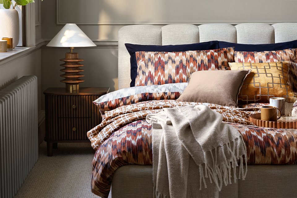 White bubble oulce bed frame with burgandy print bedding and cream throws in bedroom.
