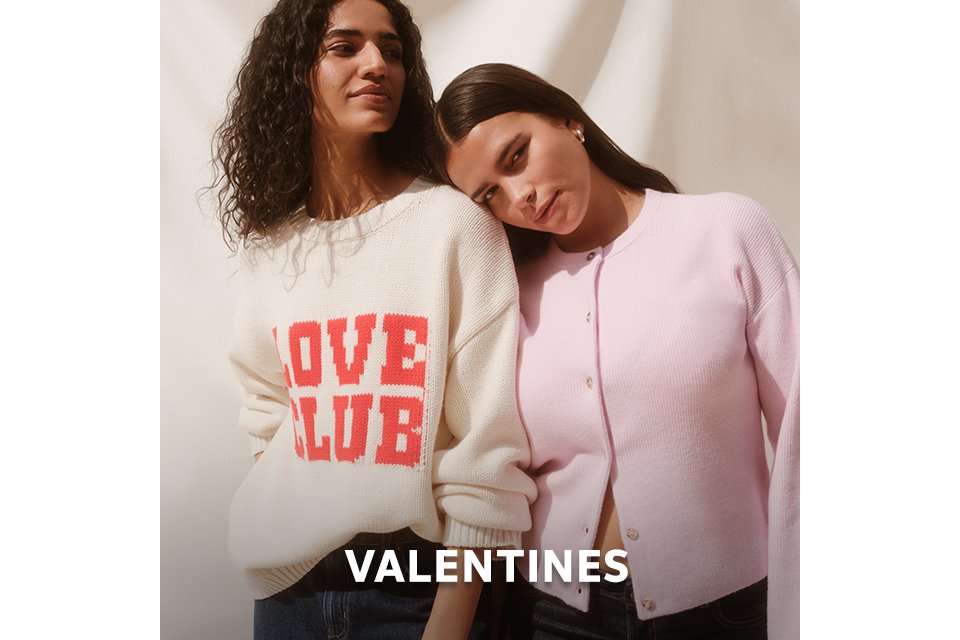 Two people wearing Valentine's themed knitwear, including a pink heart-print cardigan and a love slogan sweater. 