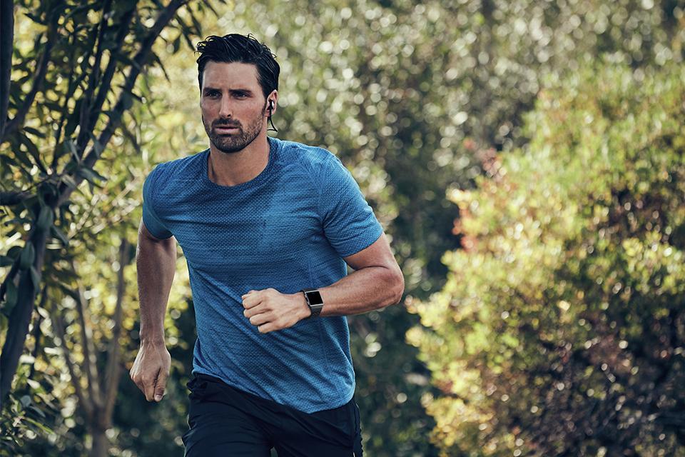 Man running outside with headphones in and a fitness tracker on his wrist.