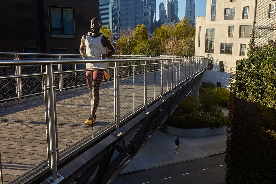 An athlete wearing Garmin Forerunner series of GPS smartwatches and running across a bridge. 