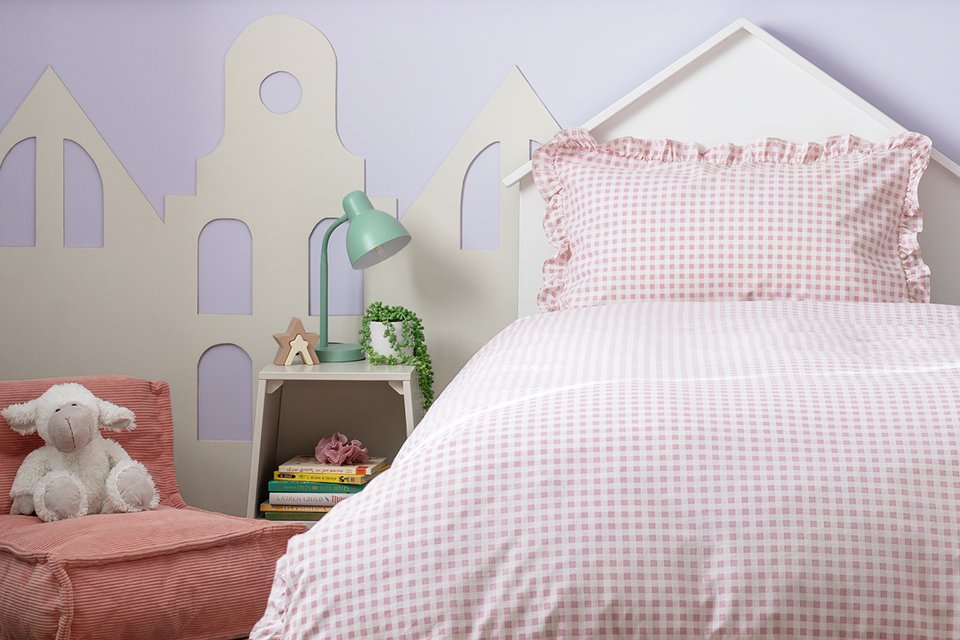 A light pink checkered bedsheet and pillow on a single bed near a side table and chair.