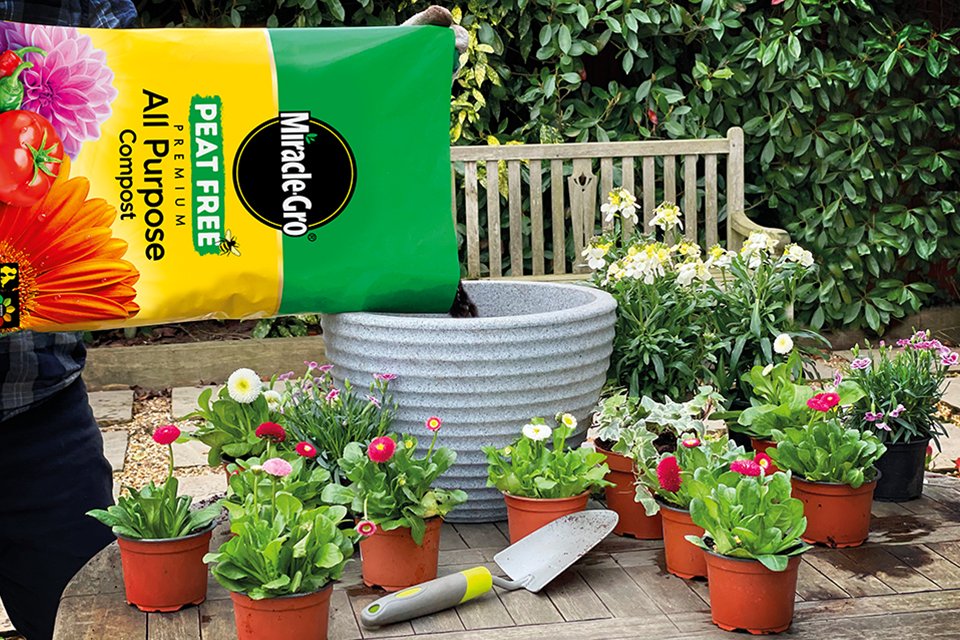 A person pouring Miracle-Gro® compost in a pot in a garden backdrop. 