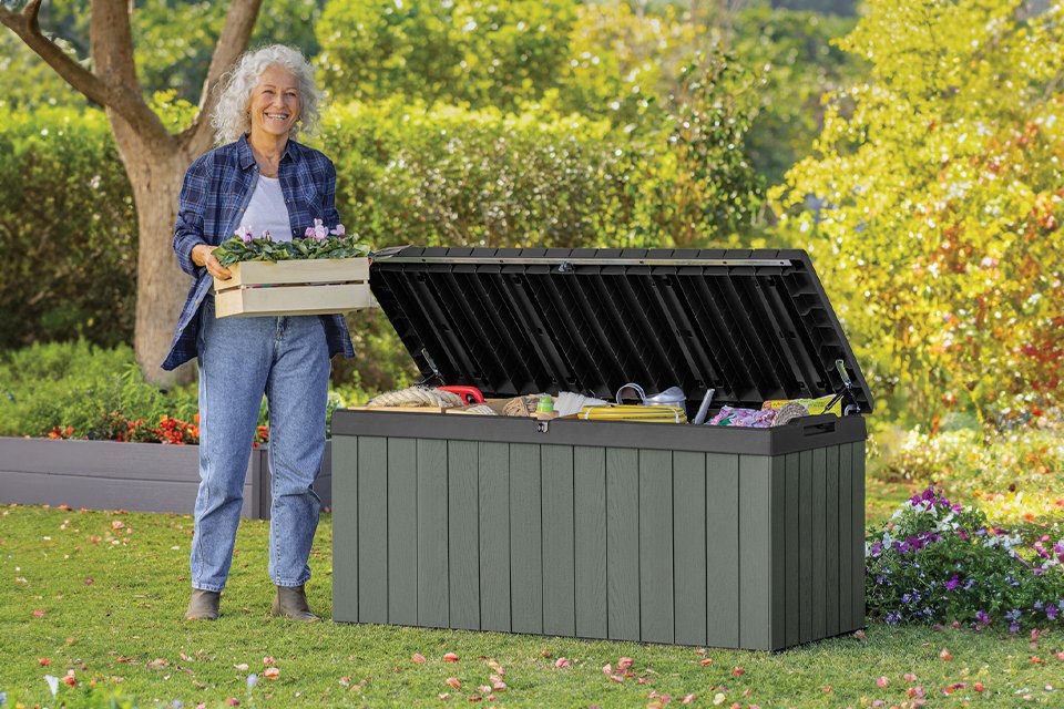 A woman standing next to a Keter Darwin 454L Outdoor Garden Storage Box in green colour.