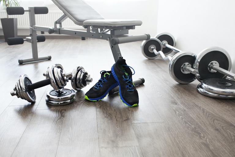 A pair of dumbbells, shoes and a weight bench in a room.