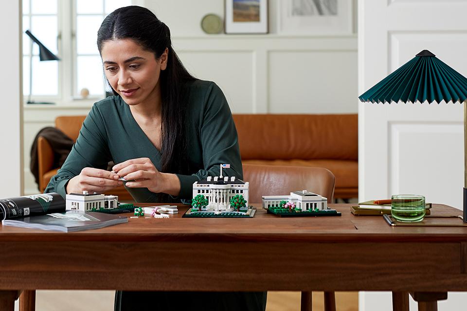 A woman sits at a wooden table, engrossed in building a LEGO® model of the White House.
