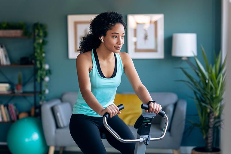 A woman doing cardio on an air bike at her home while listening to music on earpods.