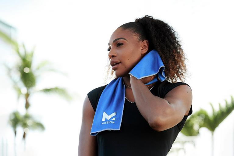 A woman using a blue coloured cooling microfibre fitness towel to wipe her sweat post workout.