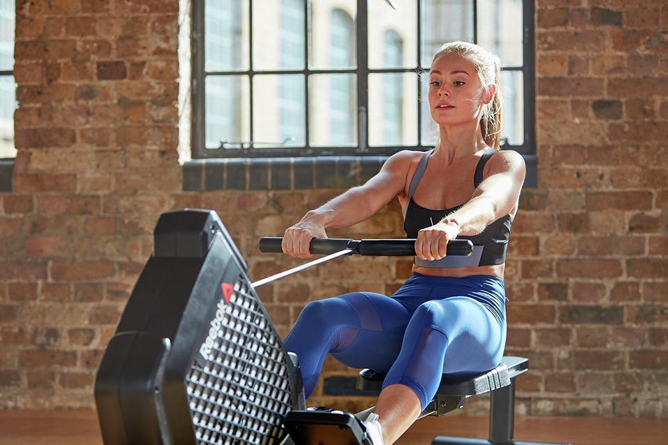 A woman using a Reebok ZJET rowing machine in a rustic gym.