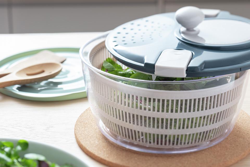 A salad spinner containing green salad leaves on a wooden dining table.
