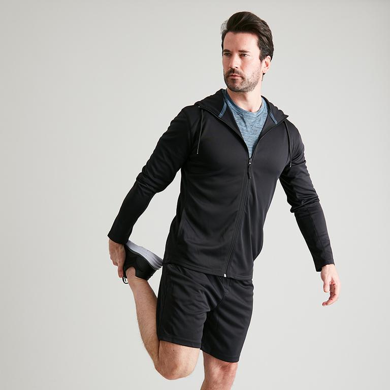 A man in a black zip-through hoodie, stretching his right leg.